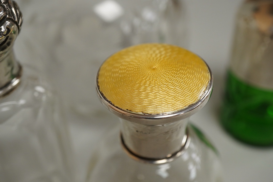 A collection of five silver mounted glass scent bottles to include one with guilloche enamel inset top, a Victorian example hallmarked for Chester 1897 and a cut glass example with mother of pearl top, London 1922, large